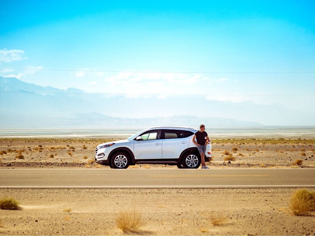 car on the side of the road with driver standing by door.