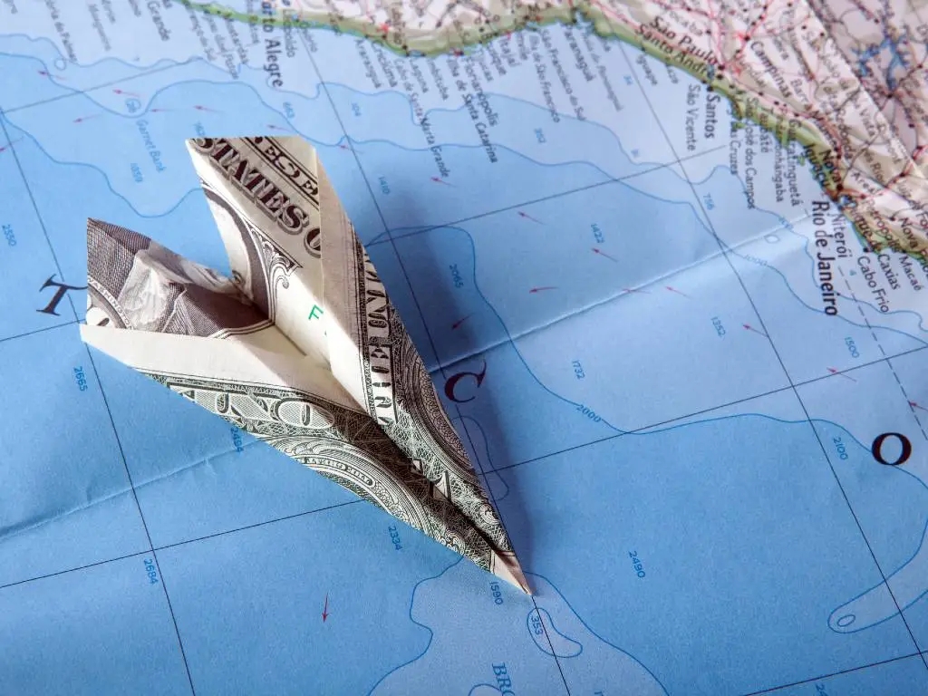paper plane made of dollar bill sitting on map.