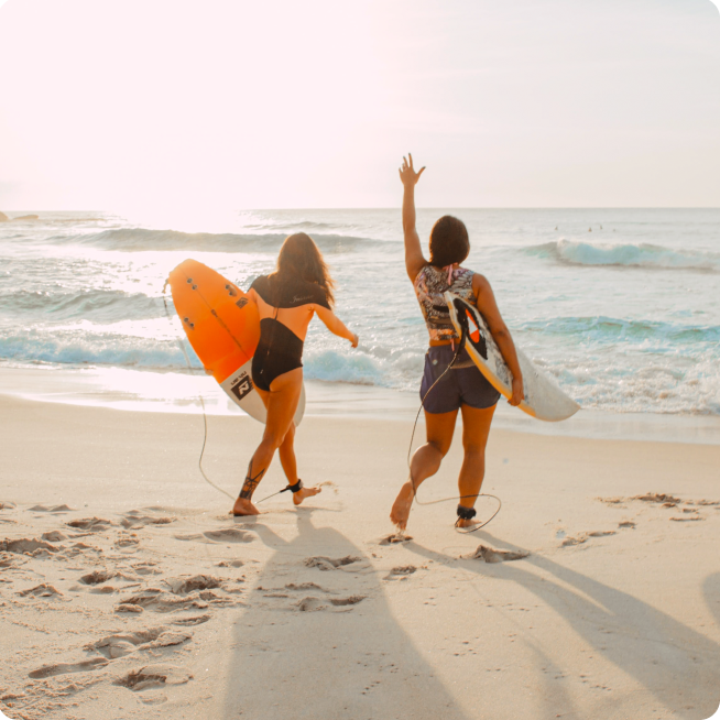 Two women walking towards the oceans carrying surfboards